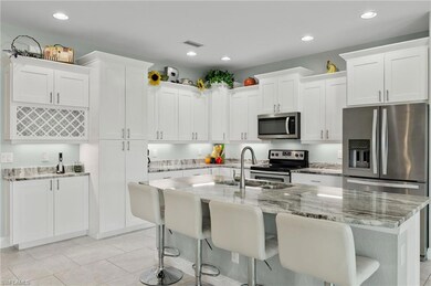 Kitchen with white cabinets, stainless steel appliances, light tile patterned floors, and an island with sink