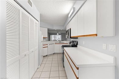 Kitchen with white cabinetry, light countertops, white appliances, light tile patterned flooring, and a textured ceiling