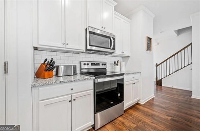 Kitchen featuring stainless steel appliances, decorative backsplash, dark wood-style floors, white cabinetry, and light stone countertops