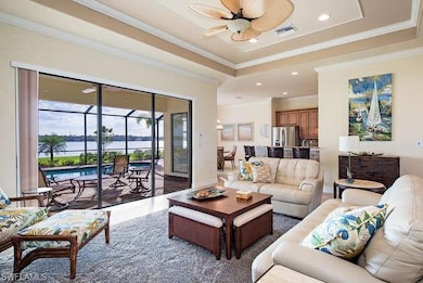 Living area featuring a tray ceiling, a water view, crown molding, recessed lighting, and a ceiling fan