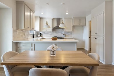 Kitchen featuring wood finished floors, tasteful backsplash, wall chimney exhaust hood, pendant lighting, and recessed lighting