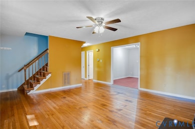 Unfurnished living room featuring stairs, light wood-style flooring, a textured ceiling, and ceiling fan