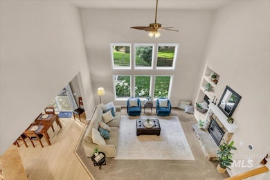Living area featuring a high ceiling, a glass covered fireplace, a ceiling fan, and wood finished floors