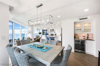 Dining space featuring ornamental molding, beverage cooler, indoor wet bar, dark wood-type flooring, and a water view