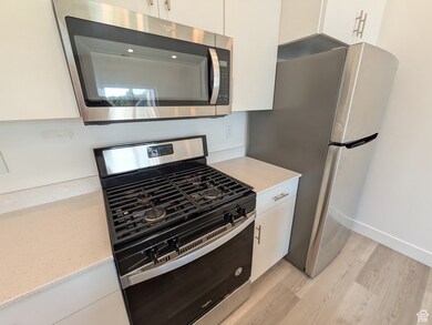 Kitchen with stainless steel appliances, white cabinets, light wood-style floors, and light quartz countertops