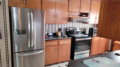 Kitchen featuring appliances with stainless steel finishes, brown cabinets, extractor fan, dark countertops, and light flooring