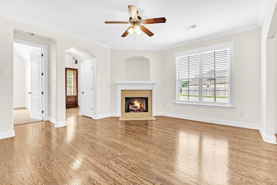Unfurnished living room with wood finished floors, ceiling fan, a fireplace with flush hearth, arched walkways, and crown molding