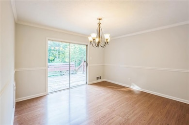 Spare room with a chandelier, wood finished floors, ornamental molding, and baseboards