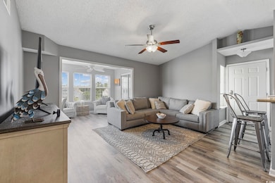 Living area with ceiling fan, wood finished floors, and a textured ceiling