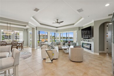 Tiled living room with plenty of natural light, a raised ceiling, ceiling fan with notable chandelier, and a water view