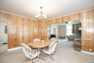 Carpeted dining area featuring arched walkways, wood walls, ceiling fan, and a chandelier