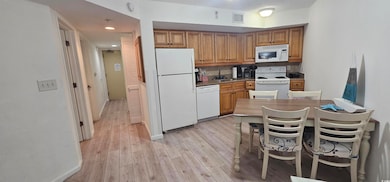 Kitchen featuring white appliances, brown cabinets, light wood-style floors, and recessed lighting