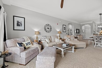 Carpeted living area featuring arched walkways, a ceiling fan, and crown molding