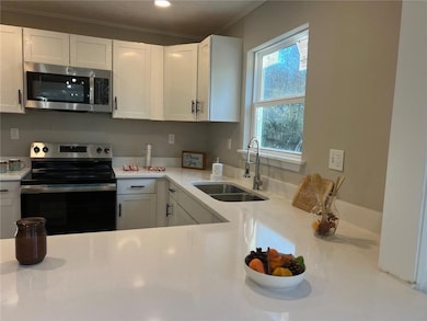 Kitchen with white cabinetry, appliances with stainless steel finishes, crown molding, and sink
