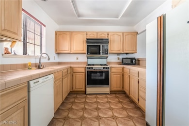 Kitchen featuring white appliances, light brown cabinets, tile countertops, and a sink