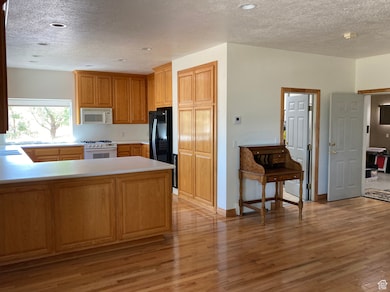 Kitchen with a textured ceiling, a peninsula, light countertops, white appliances, and light wood-style flooring