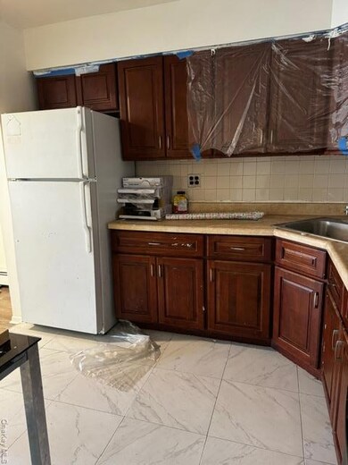 Kitchen featuring refrigerator, light countertops, light marble finish floors, and tasteful backsplash