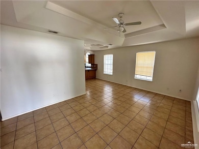 Unfurnished room featuring a raised ceiling, light tile patterned floors, a ceiling fan, and arched walkways