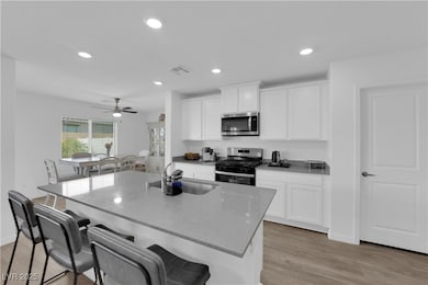 Kitchen with appliances with stainless steel finishes, light stone countertops, white cabinetry, an island with sink, and a kitchen bar