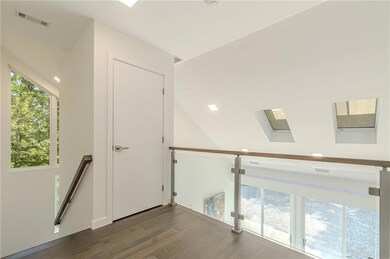 Hall featuring wood finished floors, visible vents, a skylight, and an upstairs landing