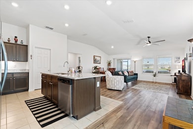 Kitchen with recessed lighting, vaulted ceiling, open floor plan, appliances with stainless steel finishes, and dark brown cabinets