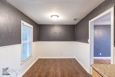 Unfurnished room with dark wood-style floors, a textured wall, and wainscoting