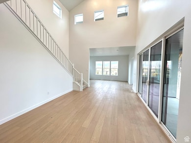 Unfurnished living room featuring stairway, a high ceiling, and light wood-style floors