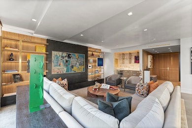 Illuminated fumed white oak shelving frame the feature wall; at right, the jewel-box bar integrates a Gaggenau wine cooler and hides storage in custom fumed white oak cabinetry.
