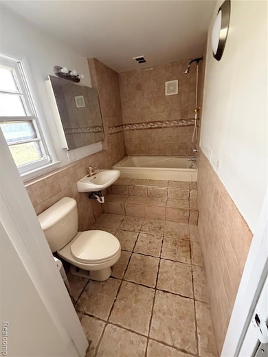 Bathroom with tile walls, light tile patterned floors, a wainscoted wall, and tiled shower / bath combo