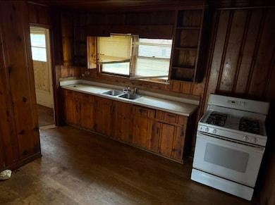 Kitchen with light countertops, white gas stove, dark wood finished floors, wooden walls, and plenty of natural light