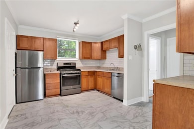 Kitchen with stainless steel appliances, tasteful backsplash, brown cabinetry, light countertops, and ornamental molding