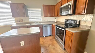 Kitchen with a sink, stainless steel appliances, brown cabinetry, and tasteful backsplash