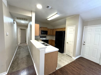 Kitchen with black appliances, light countertops, light wood-style flooring, and a peninsula