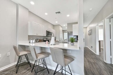 Kitchen with dark wood-type flooring, a kitchen bar, white cabinets, appliances with stainless steel finishes, and a peninsula