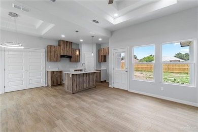 Kitchen with a raised ceiling, a sink, a kitchen island with sink, extractor fan, and brown cabinets