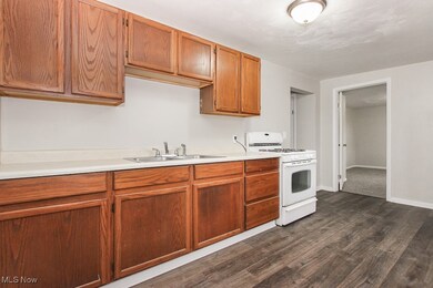 Kitchen featuring white range with gas stovetop, light countertops, dark wood-style floors, and brown cabinetry
