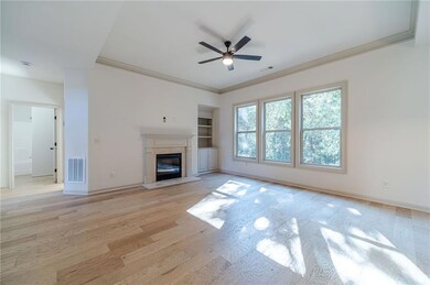Unfurnished living room featuring light wood-style floors, a fireplace with flush hearth, ornamental molding, ceiling fan, and built in shelves