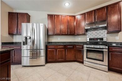 Kitchen with stainless steel appliances, under cabinet range hood, dark stone counters, and light tile patterned floors