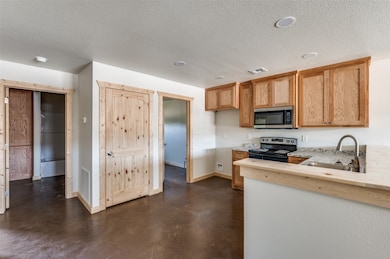 Kitchen with concrete floors, black / electric stove, a textured ceiling, stainless steel microwave, and light stone countertops