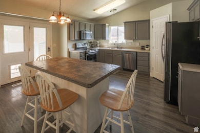Kitchen with gray cabinets, lofted ceiling, appliances with stainless steel finishes, a breakfast bar area, and hanging light fixtures
