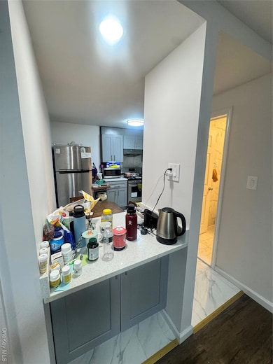Kitchen with stainless steel gas stove, refrigerator, light marble finish floors, a peninsula, and exhaust hood