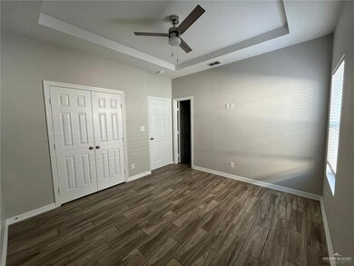 Unfurnished bedroom with a raised ceiling, dark wood-style floors, baseboards, a closet, and ceiling fan