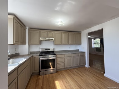 Kitchen with gas stove, light wood-type flooring, under cabinet range hood, cream cabinets, and light countertops