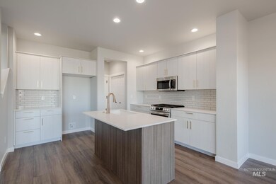 Kitchen with appliances with stainless steel finishes, white cabinetry, a kitchen island with sink, decorative backsplash, and dark wood finished floors