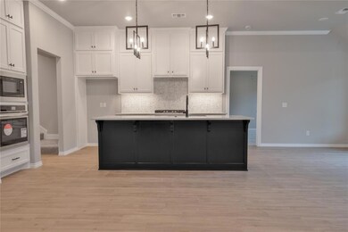 Kitchen with white cabinets, light hardwood / wood-style floors, oven, and an island with sink