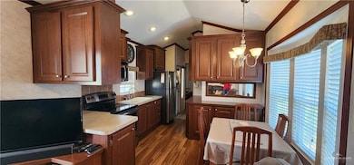 Kitchen featuring vaulted ceiling, appliances with stainless steel finishes, light countertops, dark wood-type flooring, and hanging light fixtures