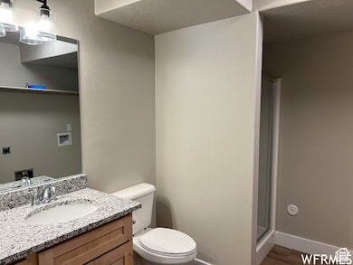 Bathroom featuring toilet, vanity, a textured ceiling, and a shower stall