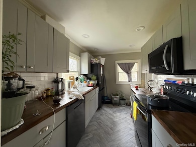 Kitchen with tasteful backsplash, black appliances, crown molding, plenty of natural light, and wood counters