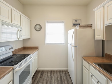 Kitchen featuring dark wood-type flooring, white appliances, sink, and white cabinets