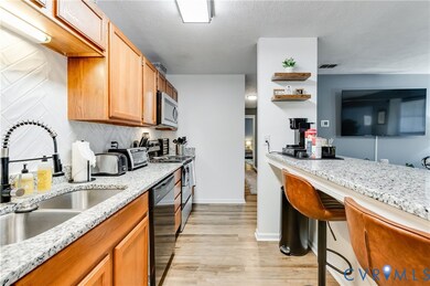 Kitchen with light wood finished floors, open shelves, black appliances, light stone counters, and a textured ceiling